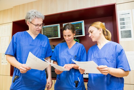 drei Ärzte in blauer Arbeitskleidung stehen zusammen und unterhalten sich. Sie halten alle ein Papier in der Hand.