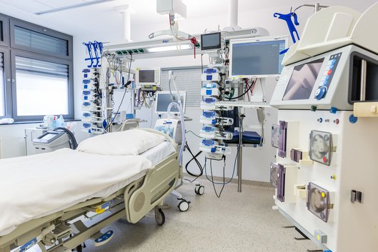In einem Patientenzimmer stehen um ein leeres Bett viele medizinisch-technische Geräte.