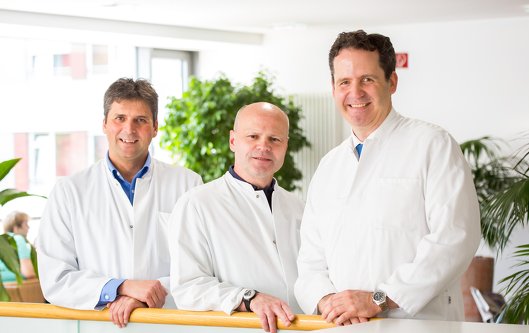 Die beiden Oberärzte Dr. Sattlegger und Dr. Höfges stehen links neben Chefarzt Privat-Dozent Dr. Utech. Sie tragen alle einen weißen Arztkittel.