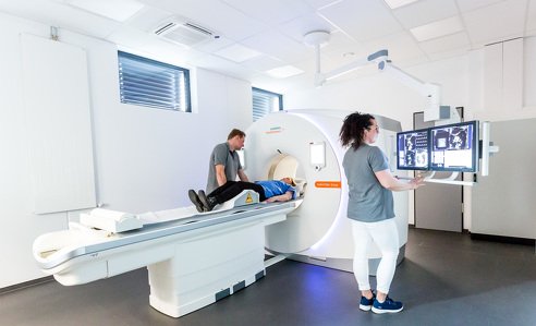 Eine Patientin liegt zur Untersuchung im CT. Zwei Praxismitarbeiter bereiten die Aufnahmen vor.